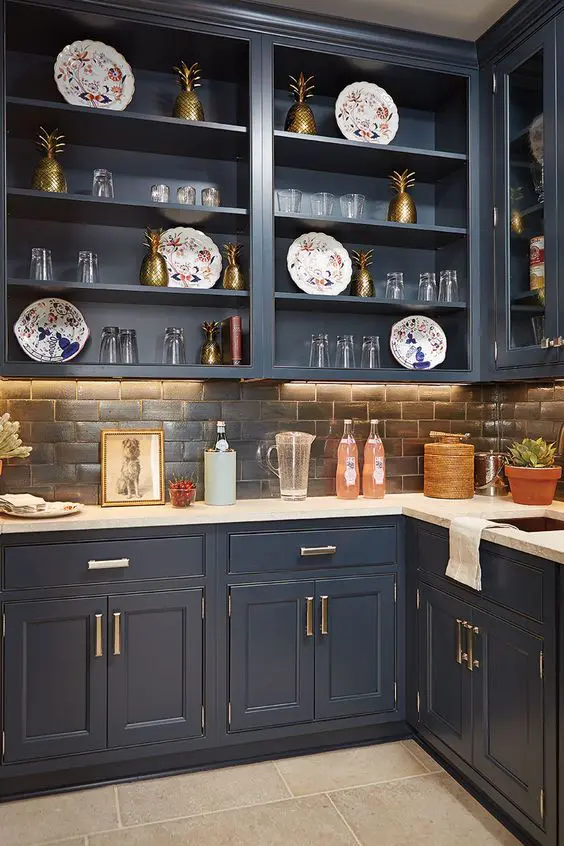 a refined navy kitchen with shaker and open cabinets, a dark tile backsplash and white countertops, brass and gold touches