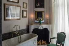 a refined vintage bathroom with a chic French fireplace, a marble bathtub, a black chandelier, a gallery wall and a green chair