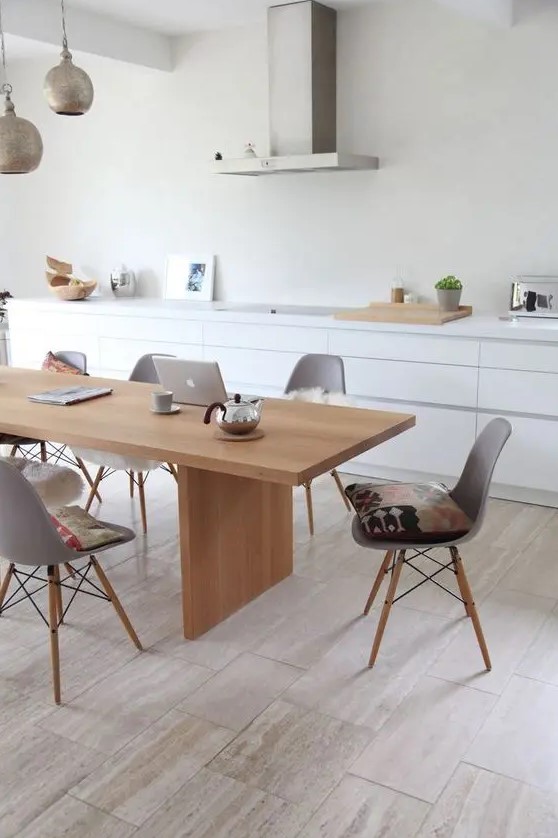 A sleek Nordic dining room with a light stained table and grey Eames chairs plus metal pendant lamps