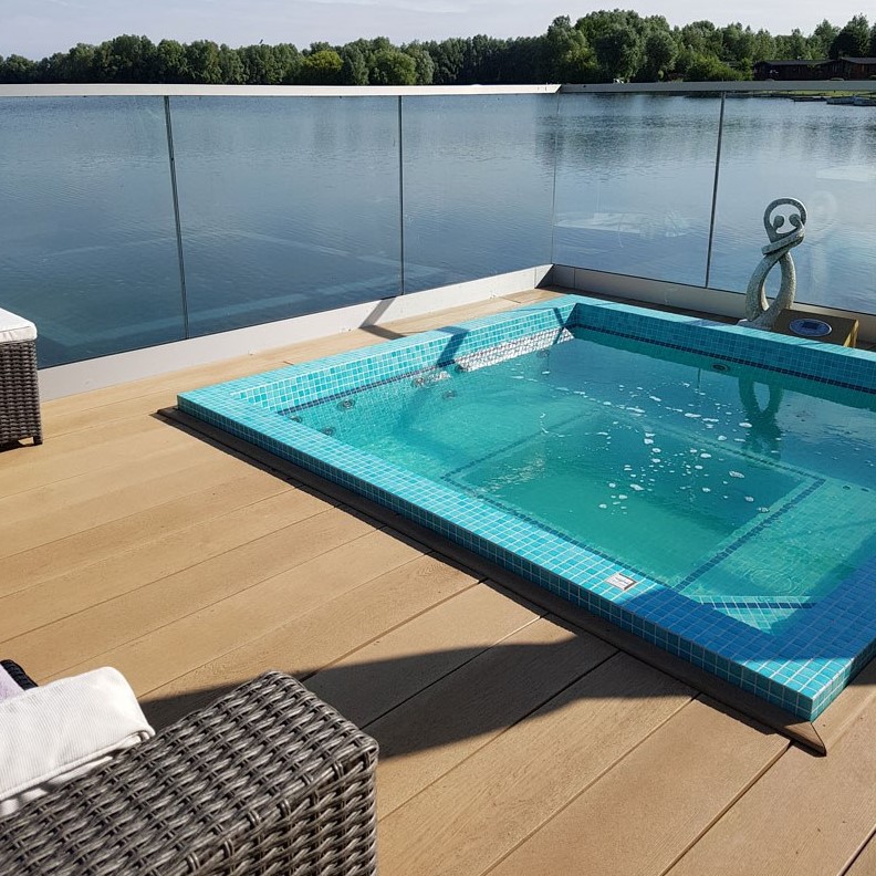 a small deck clad with gold oak millboard, a jacuzzi, woven furniture and glass banister that doesn't prevent from enjoying the vies