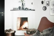 a small fireplace nook with a brown leather butterfly chair, a black side table, a basket and a bucket with wood, a gallery wall