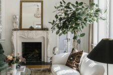 a sophisiticated neutral space with a French fireplace, a white curved sofa, an oval coffee table, a potted plant