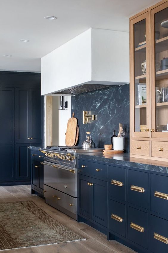 a sophisticated black and white kitchen with stained cabinets, black soapstone countertops and a backsplash and gold fixtures