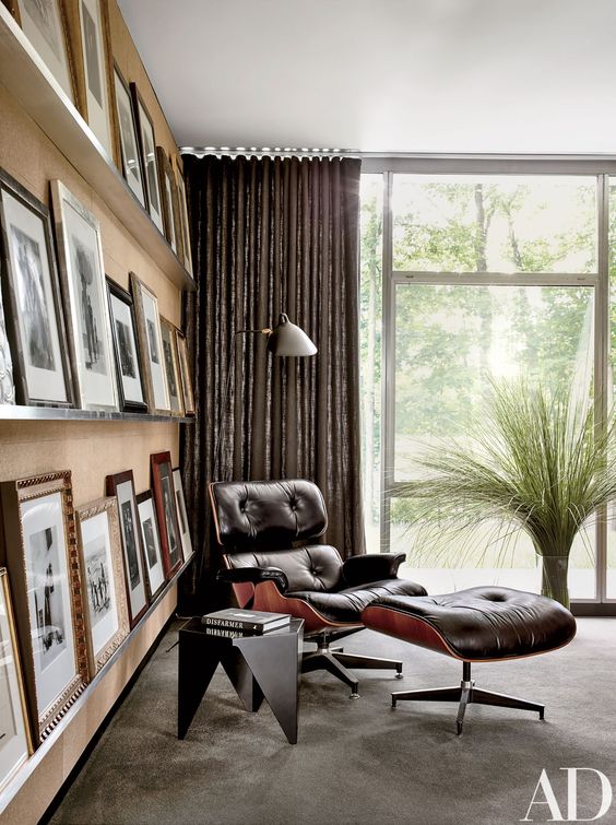 A stylish mid century modern nook with a black Eames lounger and ottoman, a black side table and three ledges presenting a gallery wall