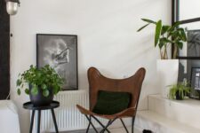 a stylish modern nook with a glass wall and a ladder with potted plants, a brown leather butterfly chair, a bold rug