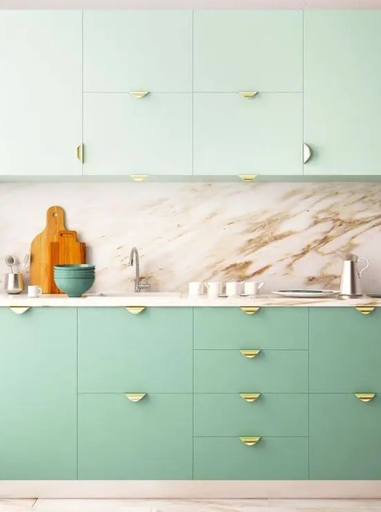A two tone kitchen with mint green and brighter green cabinets, a marble backsplash and countertops, gold pulls is amazing