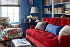 a vibrant space with blue walls, built-in bookshelves, a red sofa and a floral chair, layered rugs and an acrylic table