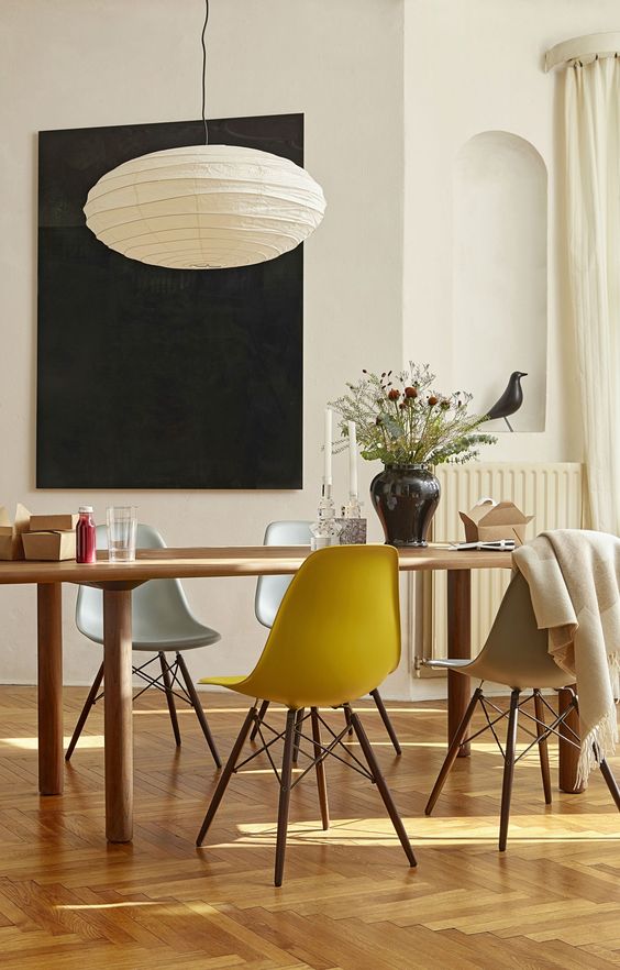 a welcoming dining space with a dining table and muted color Eames chairs, a paper pendant lamp and some dried flowers