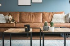 a welcoming living room with blue walls, a gallery wall, wooden tables and a sectional brown leather sofa