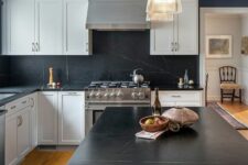 a white farmhouse kitchen with shaker cabients, a black soapstone backsplash and countertops, a stained kitchen island and chic pendant lamps