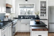 a white farmhouse kitchen with shaker cabinets, black soapstone countertops and a backsplash, touches of stained wood