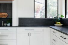 a white farmhouse kitchen with shaker cabinets, black soapstone countertops and a backsplasj, skinny tiles and black fixtures