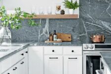 a white shaker style kitchen with open shelves, grey soapstone countertops and a backsplash, lots of greenery