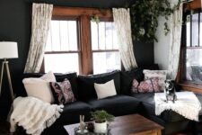 an eclectic living room with a black accent wall, a black sectional, stained window frames and an echoing coffe table and neutral textiles