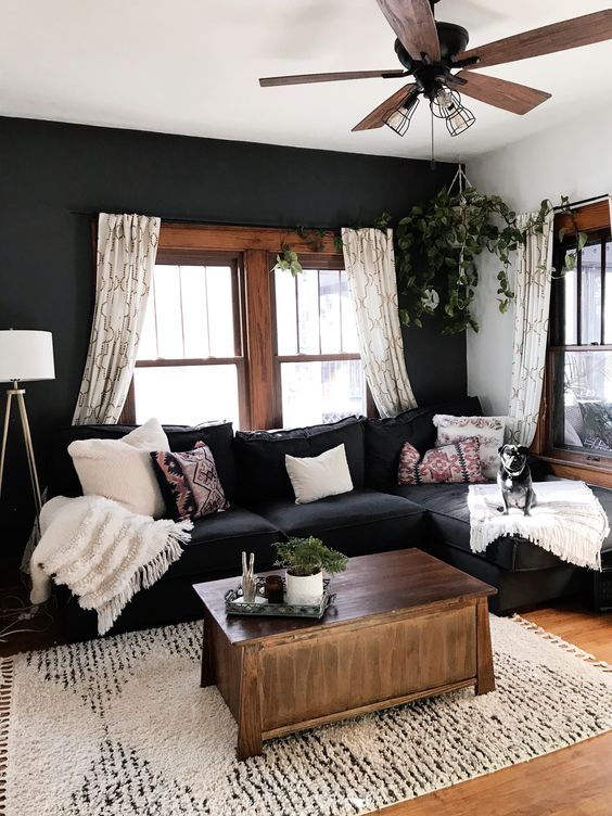 an eclectic living room with a black accent wall, a black sectional, stained window frames and an echoing coffe table and neutral textiles