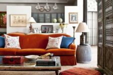 an eclectic living room with a burnt orange sofa, a low table and pretty tassel cushions and a table lamp