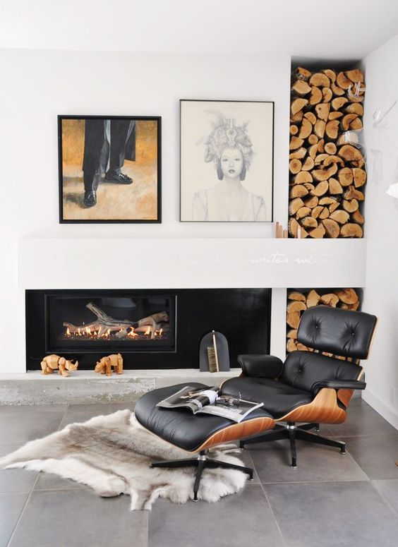 an elegant fireplace nook with a built-in fireplace, a black Eames lounger and an ottoman, a rug, a firewood storage niche