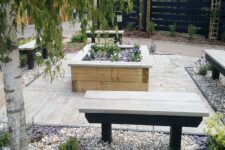 an outdoor space with weathered oak decking, benches, a flower bed with blooms, pebbles and trees