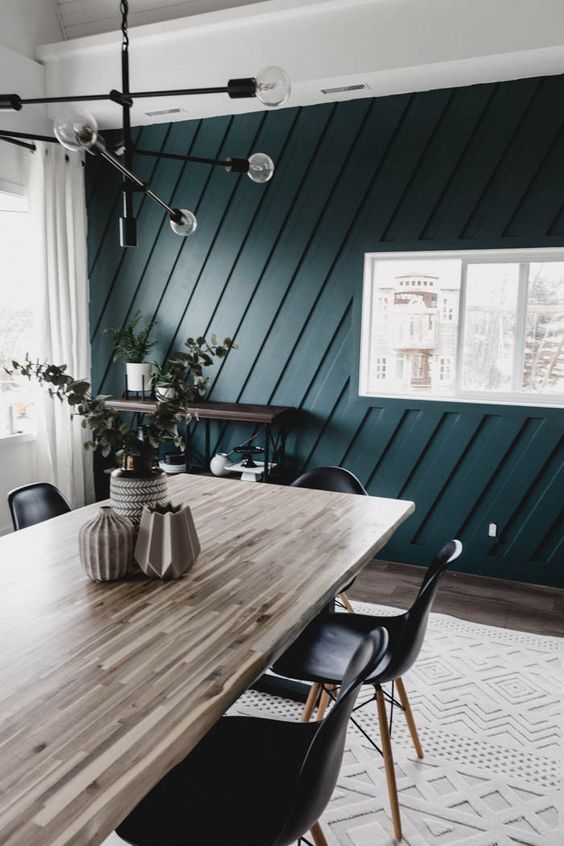 a beautiful farmhouse dining room with a butcherblock dining table, black Eames chairs, a black chandelier, a teal paneled accent wall that wows