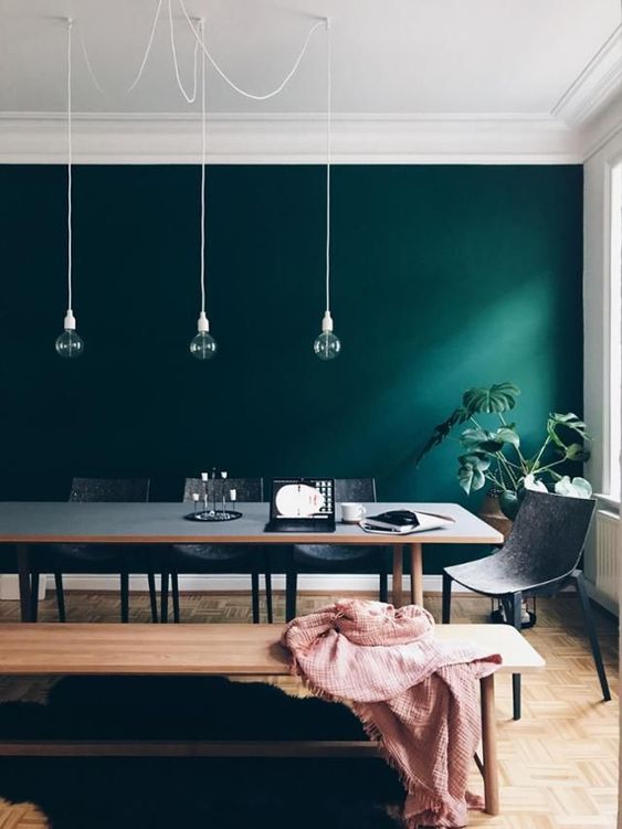 a Scandinavian dining space with a dark green accent wall, a grey table and chair, pendant bulbs is chic and cool