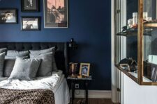 11 an attic bedroom with a navy accent wall and a gallery wall, a black upholstered bed, a glass shelving unit on the wall