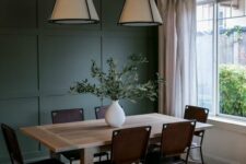 12 a cool dining room with a dark green paneled wall, a butcherblock table, brown chairs, pendant lamps and neutral curtains