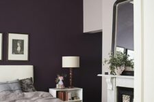 14 a chic bedroom with a deep purple accent wall, a white upholstered bed, grey bedding, a non-working fireplace, a mirror and a crystal chandelier