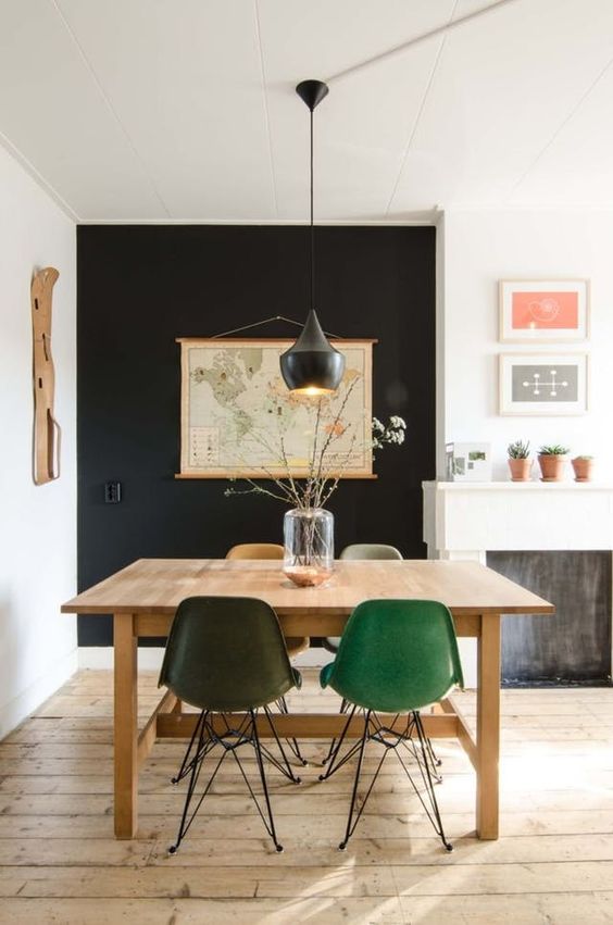 a cozy dining space with a black accent wall, a stained table and colored chairs, a black pendant lamp and a map on the wall