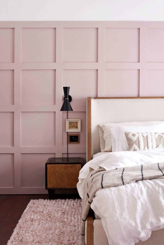 a chic bedroom with a pink paneled wall, a white bed, dark nightstands and sconces plus neutral embroidered bedding