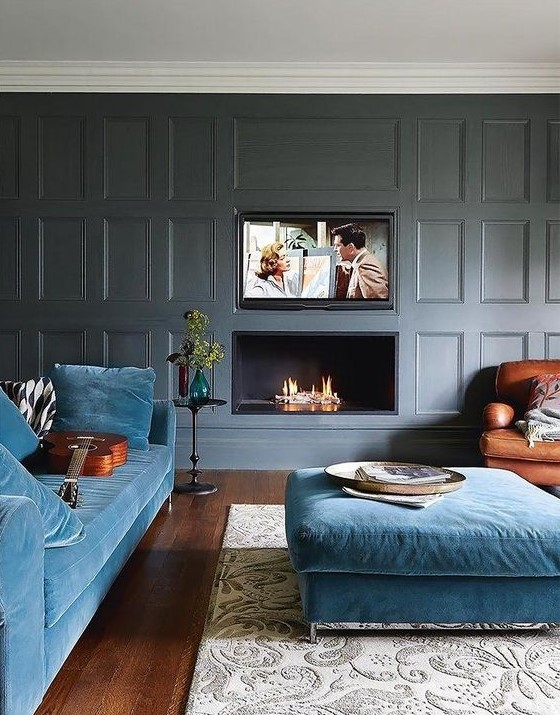 A modern luxurious living room with grey paneled walls, blue furniture and a built in fireplace and TV