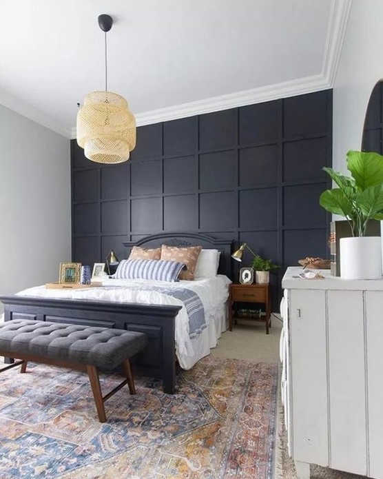 a stylish bedroom in modern and boho styles, with a black paneled wall, a black bed and a grey bench plus a wicker lamp