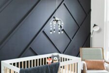 25 a catchy nursery with a black paneled wall, a crib, a rocker and some printed textiles and a mobile