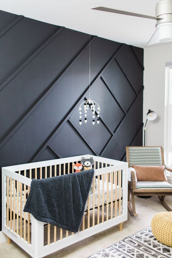a catchy nursery with a black paneled wall, a crib, a rocker and some printed textiles and a mobile