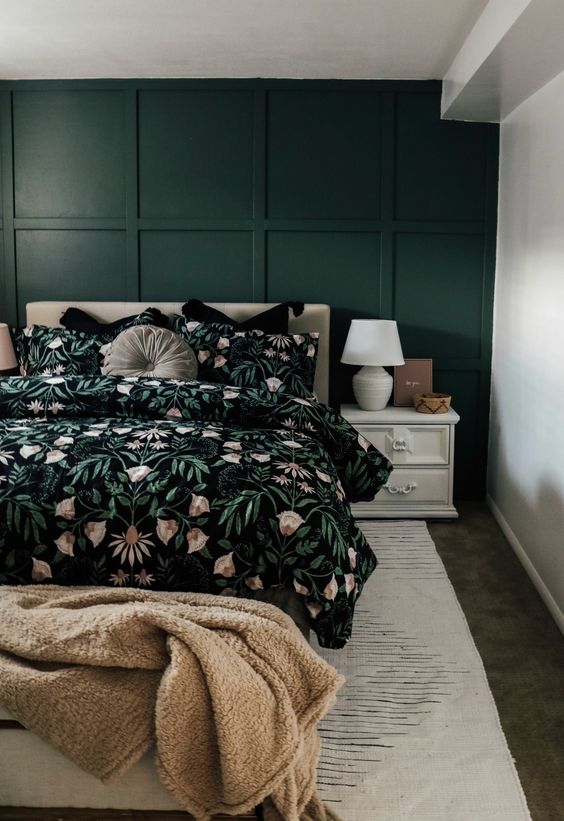 a beautiful guest bedroom with a dark green paneled wall, a neutral upholstered bed with bold floral bedding, white nightstands
