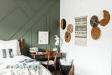 28 a cool boho bedroom with a green paneled wall, a bed with neutral bedding, a bench, a mini desk, a lovely gallery wall with platters