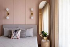 30 a glam bedroom with a pink paneled wall, a grey bed with grey bedding, an oval mirror, gold sconces and neutral curtains
