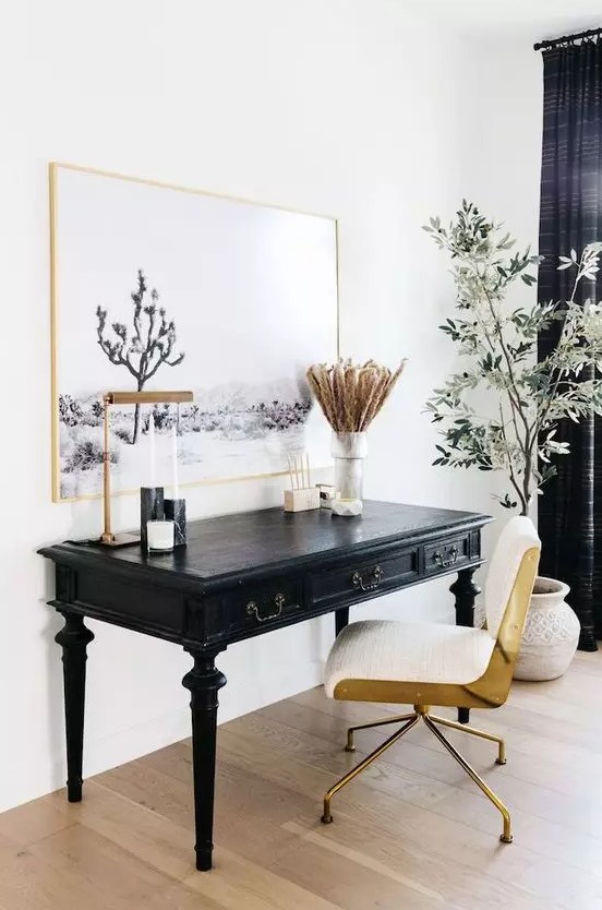 a beautiful home office with a vintage black desk, a modern gold and white chair, a statement artwork and a potted plant