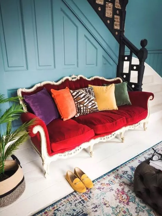 a bright eclectic entryway finished off with a bold vintage red sofa that stands out and colorful pillows