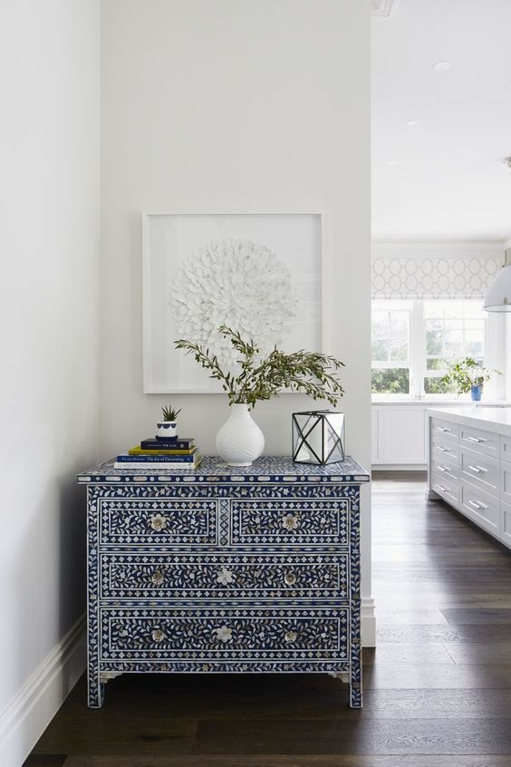 A jaw dropping navy and white inlay sideboard with a book stack, some greenery and a candle lantern makes an accent in the space