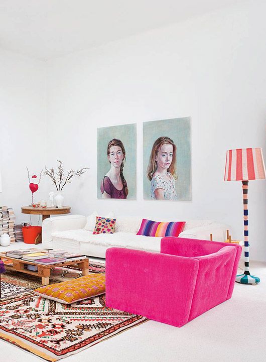 a colorful eclectic living room with a white low sofa, a hot pink chair that makes a statement, a bold boho rug, a pallet coffee table