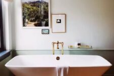 51 a chic and peaceful bathroom with green paneling, a catchily shaped bathtub, gold fixtures and a mini gallery wall with photos
