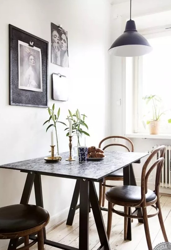 a cool Scandinavian dining space with a trestle and black chairs, a black and white gallery wall and a black pendant lamp
