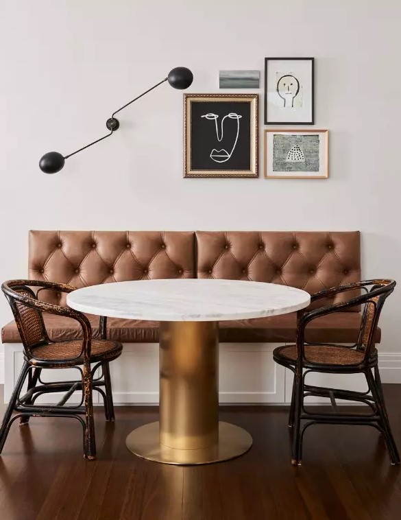 a refined dining space with a banquette seating, a round table, rattan chairs, a mini gallery wall and a black sconce