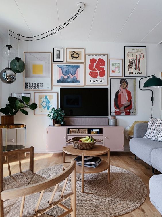 a fantastic living room with a colorful gallery wall, a pink TV unit, a grey sofa, wooden chairs and a coffee table, pendant lamps