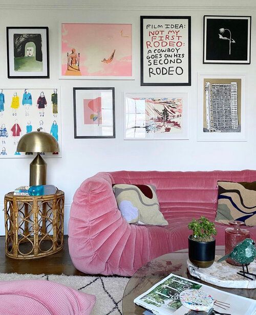 a cool and bright living room with pink seating furniture, a coffee table, a rattan side table and a colorful gallery wall
