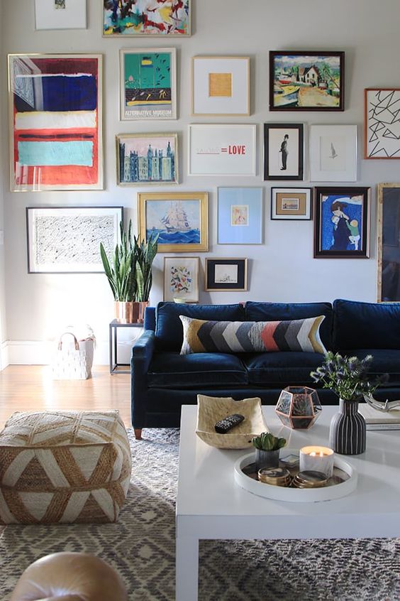 a catchy living room with a navy sofa and bright pillows, a printed pouf and rug, a colorful gallery wall and potted plants