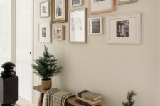 60 a farmhouse entryway with a wooden bench, a chic black and white gallery wall, sconces and potted fir trees
