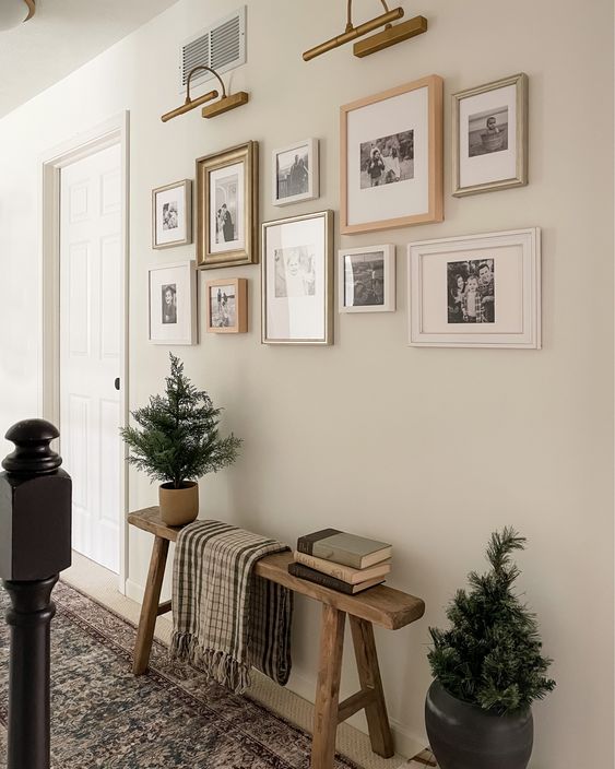 a farmhouse entryway with a wooden bench, a chic black and white gallery wall, sconces and potted fir trees