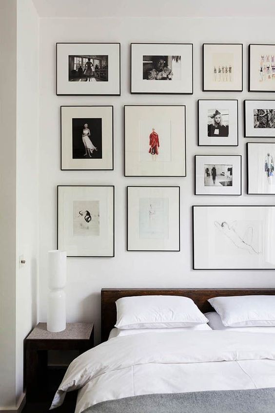 An airy bedroom with a dark stained bed and nightstands, grey and white bedding, a large gallery wall over the headboard