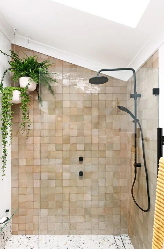 an attic shower space clad with blush and tan Zellige tiles, with suspended potted plants and black fixtures for a modern feel